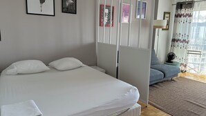 A bedroom with a bed, a sofa, a window with curtains, and wall art. - Spacious 2-room apartment with parking in Paris La Défense overlooking the Eiffel Tower   (Puteaux)