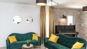 Ein Wohnzimmer mit zwei grünen Sofas, einem kleinen runden Tisch, einem Blumentopf und einem Klavier an einer Ziegelwand.