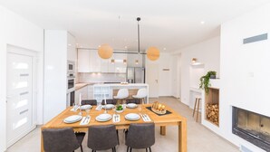 Eine moderne Küche mit weißen Schränken, einem Holzespeisetisch, der für vier Personen gedeckt ist, und einem Kamin mit brennendem Holzfeuer.
