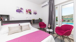 Ein modernes Hotelzimmer mit einem großen Bett, einem Schreibtisch, zwei Stühlen und Blick auf einen Pool und Hügel.