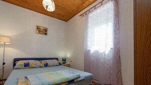 A bedroom with a bed, a bedside table, a lamp, a window with curtains, and a wooden ceiling. - Three Bedroom Holiday Home (Vinisce)