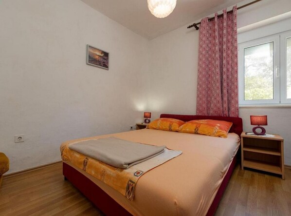 Un dormitorio con cama, mesitas de noche, una ventana con cortinas, una lámpara de pared y una pequeña foto en la pared.