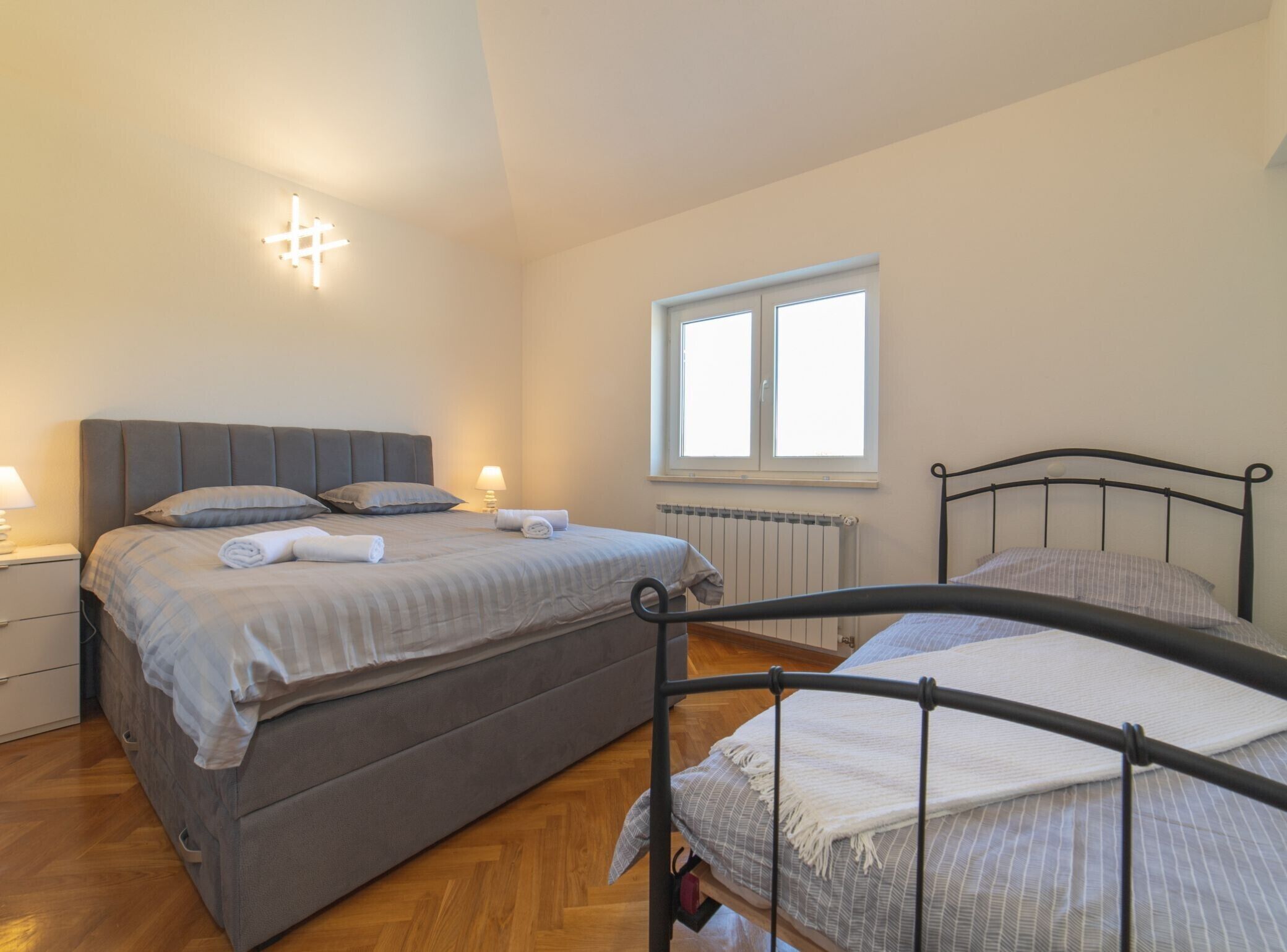 A bedroom with two beds, a window, a radiator, and bedside lamps.