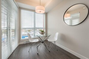 Ein modernes Zimmer mit Glastisch und Stühlen, einem runden Spiegel und Blick durch große Fenster.