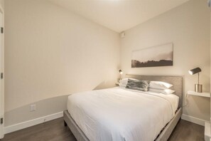 Ein Schlafzimmer mit einem Bett, einem Nachttisch, einer Wandlampe und einem gerahmten Bild.