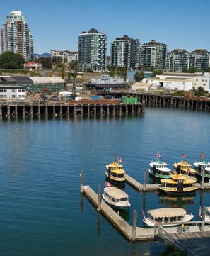A marina with several boats docked, a pier extending into calm water, and a cityscape with high-rise buildings in the background. - Modern Old Town Suite with Private Balcony (Victoria Central British Columbia Provincial Government)