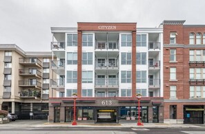 Ein mehrstöckiges Gebäude mit der Aufschrift "CITYZEN" auf der Fassade. Es hat einen modernen architektonischen Stil und Balkone in den oberen Etagen. Der Eingang ist mit der Nummer "613" gekennzeichnet.
