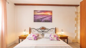 A bedroom with a bed, two bedside tables, a nightstand, a wall-mounted painting, and a wooden headboard. - Serene Retreat Holiday Home with Pool - Two Bedroom Holiday Home (Veliki Brocanac)