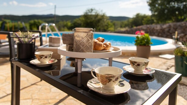 A table set with tea cups, saucers, a teapot, and pastries by a poolside with a scenic view. - Serene Retreat Holiday Home with Pool - Two Bedroom Holiday Home (Veliki Brocanac)