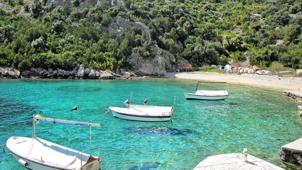 A coastal scene with boats docked at a pier, clear turquoise water, and a rocky hillside in the background. - Sea-View Apartments with Pool, Terrace, and Outdoor Lounge in Scenic Čiovo Island - Comfort One Bedroom Apartment (Ciovo)