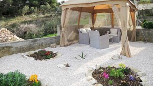 An outdoor seating area with a canopy, surrounded by gravel and plants. - Sea-View Apartments with Pool, Terrace, and Outdoor Lounge in Scenic Čiovo Island - Comfort One Bedroom Apartment (Ciovo)