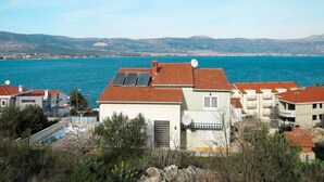 A coastal residential area with houses featuring red-tiled roofs and solar panels, overlooking a large body of water and distant hills. - Sea-View Apartments with Pool, Terrace, and Outdoor Lounge in Scenic Čiovo Island - Comfort One Bedroom Apartment (Ciovo)