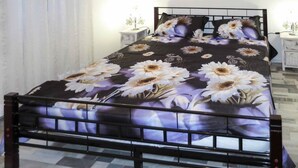 A bed with a floral bedspread, a bedside table with a lamp, and a wall-mounted hanging. - Sea-View Apartments with Pool, Terrace, and Outdoor Lounge in Scenic Čiovo Island - Two Bedroom Apartment (Ciovo)