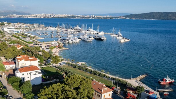 Una marina con numerosos yates amarrados, una zona de playa con gente y un paisaje urbano al fondo.