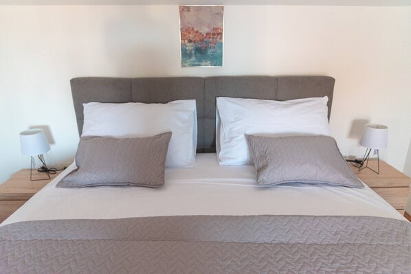 A double bed with a grey headboard and white bedding, flanked by two bedside tables with lamps.