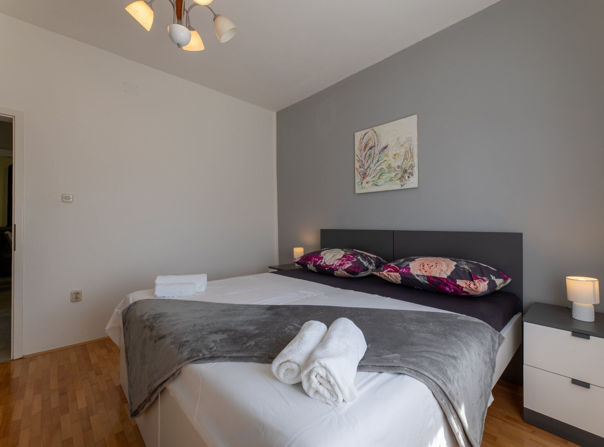A modern bedroom with a bed, a nightstand, a wall-mounted lamp, and a painting.