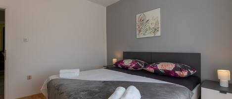 A modern bedroom with a bed, a nightstand, a wall-mounted lamp, and a painting.