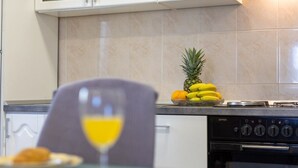 Eine Küche mit weißen Schränken, einem Herd und einer Obstschale mit Ananas, Bananen und Orangen.