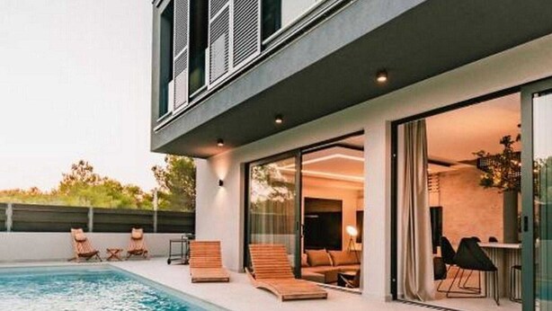 A modern house with a swimming pool, outdoor seating, and a glass door leading to the interior. - Four Bedroom Villa with pool (Vodice)