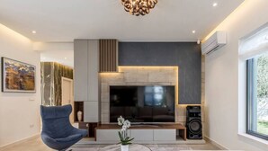 A modern living room with a large flat-screen TV, a comfortable sofa, a coffee table, and a speaker.