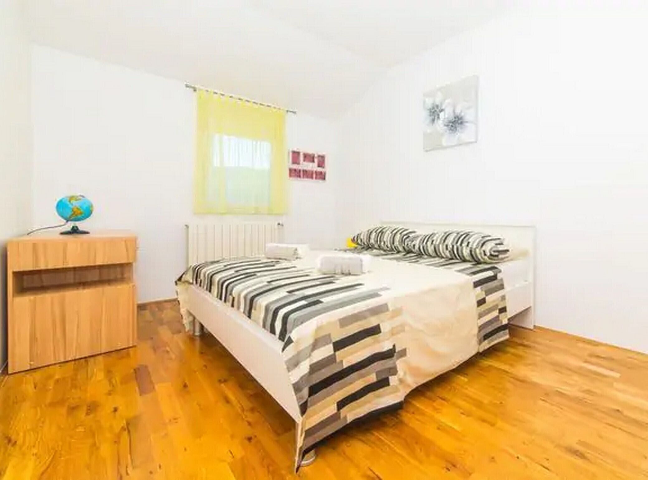 Quarto com cama, penteadeira de madeira, globo, radiador e janela com cortina amarela.