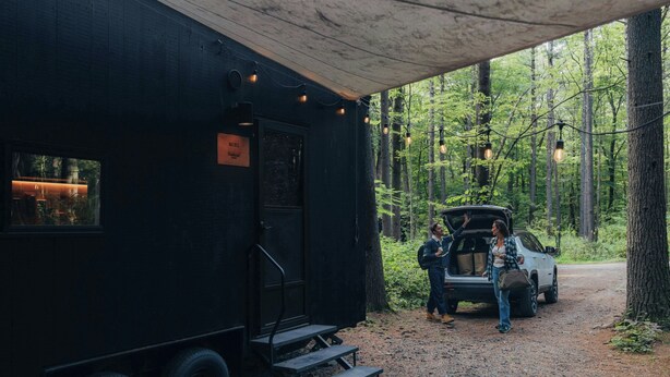 Un camping-car noir doté d’une terrasse en bois et d’un escalier menant à une zone abritée.