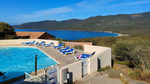 A pool area with blue lounge chairs, a clear view of a lake, and a mountainous landscape in the background.