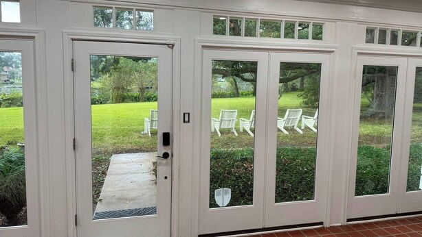 Une paire de portes doubles blanches, dotées de panneaux de verre, qui donnent sur un patio aménagé avec une pelouse et des chaises.