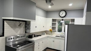 Une cuisine moderne avec des meubles blancs, des appareils en acier inoxydable, une horloge et une fenêtre donnant sur un paysage verdoyant.