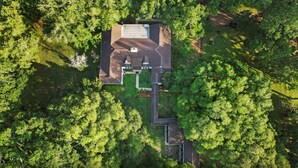 Une vue aérienne d’une maison entourée d’une forêt dense, avec une allée bien dégagée menant à l’entrée.