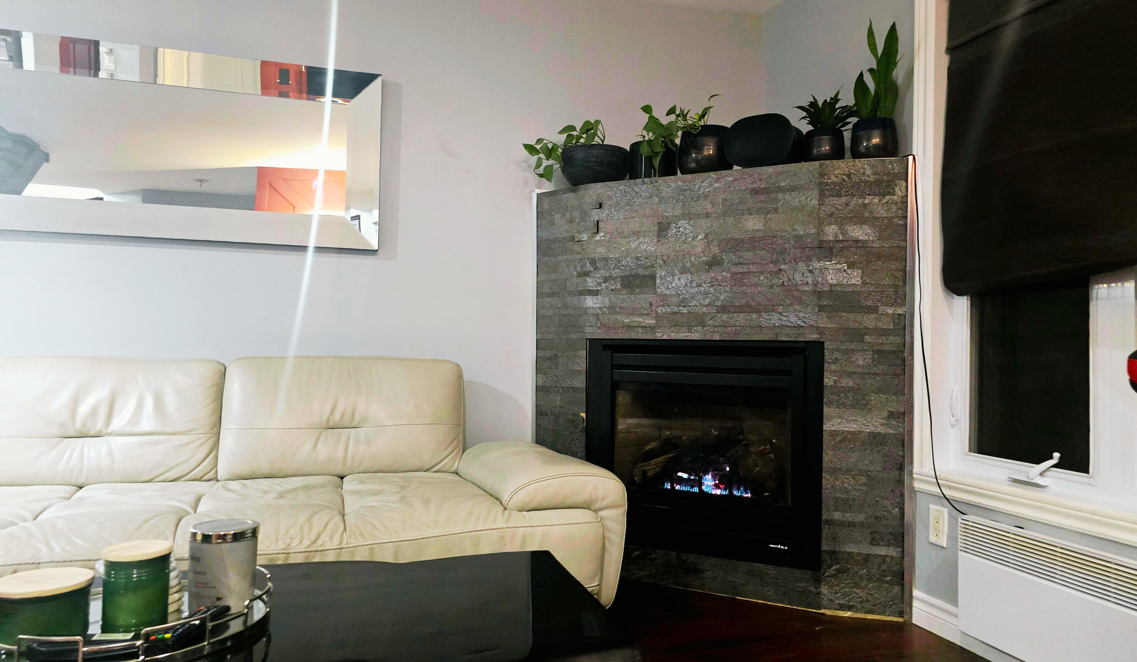 A living room with a beige sofa, a fireplace with a stone facade, and a window with blinds.