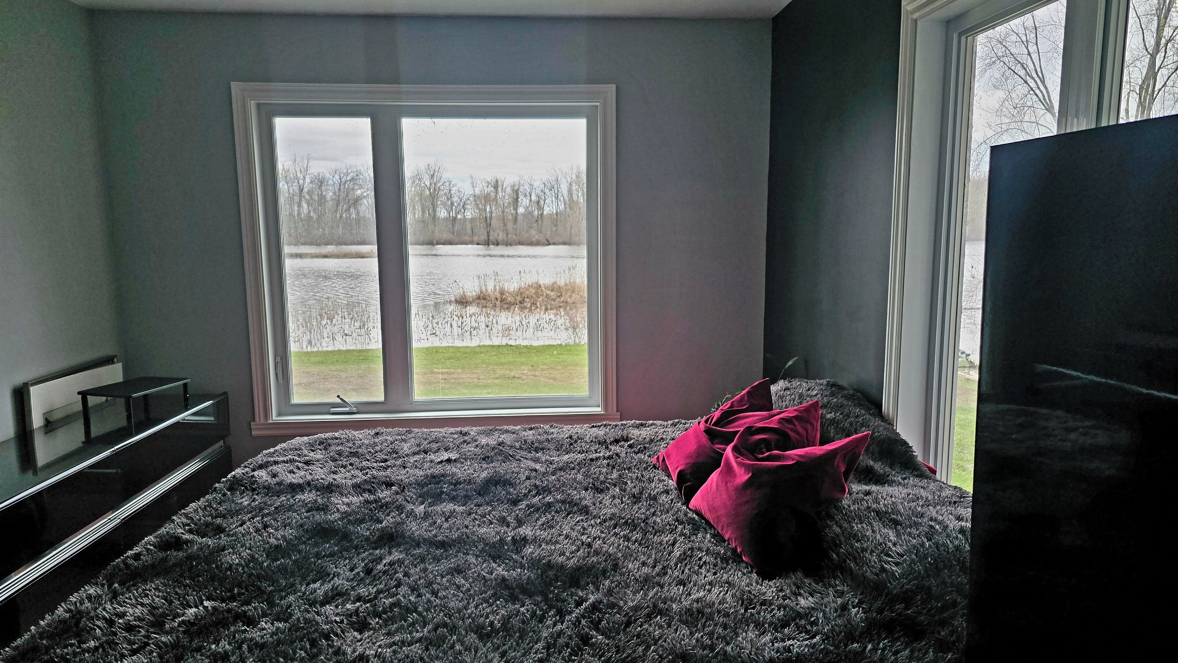 A bedroom with a large window, a bed with a fluffy gray blanket, and a pink pillow.