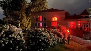 Una casa de ladrillo con varias ventanas y un jardín bien cuidado con flores blancas.