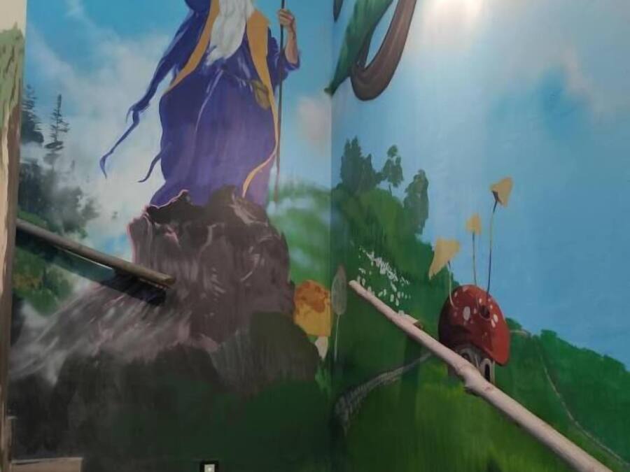 Un mural que muestra a un mago en una rama de árbol, con una varita, un hongo rojo y un cielo azul.