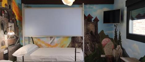 A room with two beds, a mural of a castle, a mounted TV, and a wooden desk.