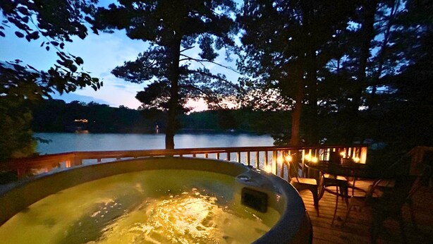 A hot tub on a wooden deck with a lake view at dusk.