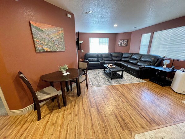 Un salon avec un canapé en cuir marron foncé, une table à manger avec des chaises, une table basse et un tableau accroché au mur.