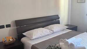 A neatly made bed with white linens, a dark headboard, and a small bedside table with a basket of toiletries. - One stop away from FCO Airport and Fiera di Roma. Complete with all amenities (Lazio)