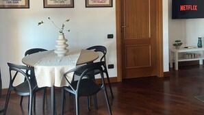 A dining area with a round table, chairs, and a vase of flowers. There are three framed posters on the wall and a television on a stand. - One stop away from FCO Airport and Fiera di Roma. Complete with all amenities (Lazio)