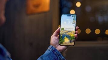 Una persona sostiene un teléfono inteligente que muestra un mensaje sobre una escapada a la naturaleza y una cabaña con vistas panorámicas.
