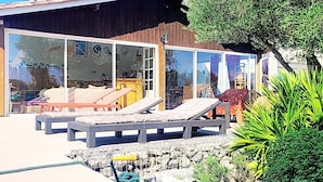 Ein modernes Haus mit großen Glasfenstern, Sitzgelegenheiten im Freien und einem Kiesweg.