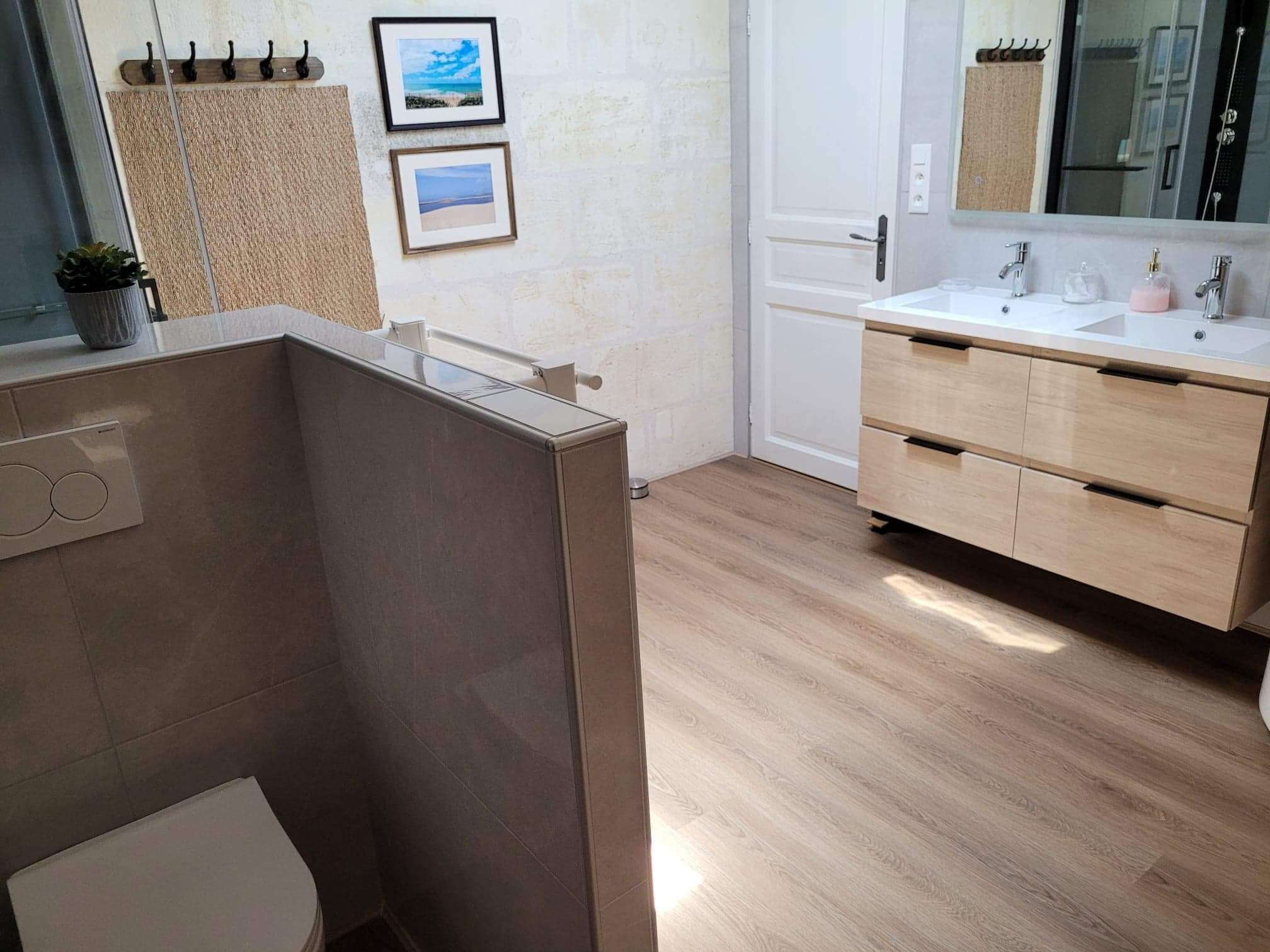 Ein modernes Badezimmer mit einem Holzbadezimmerhocker, einem großen Spiegel und zwei gerahmten Bildern an der Wand.