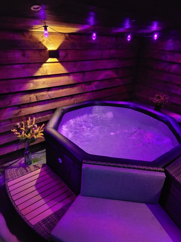 A hot tub with a wooden exterior, surrounded by a wooden deck and a small flower arrangement.