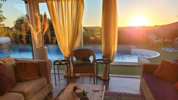 Ein gemütlicher Innenbereich mit Sitzgelegenheit und Blick auf einen Swimmingpool bei Sonnenuntergang.