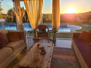 A cozy indoor seating area with a view of a swimming pool at sunset.