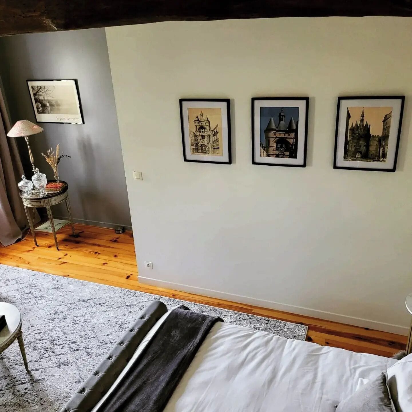 Et soveværelse med en seng, et lille bord med en lampe og tre billeder i rammer på væggen.