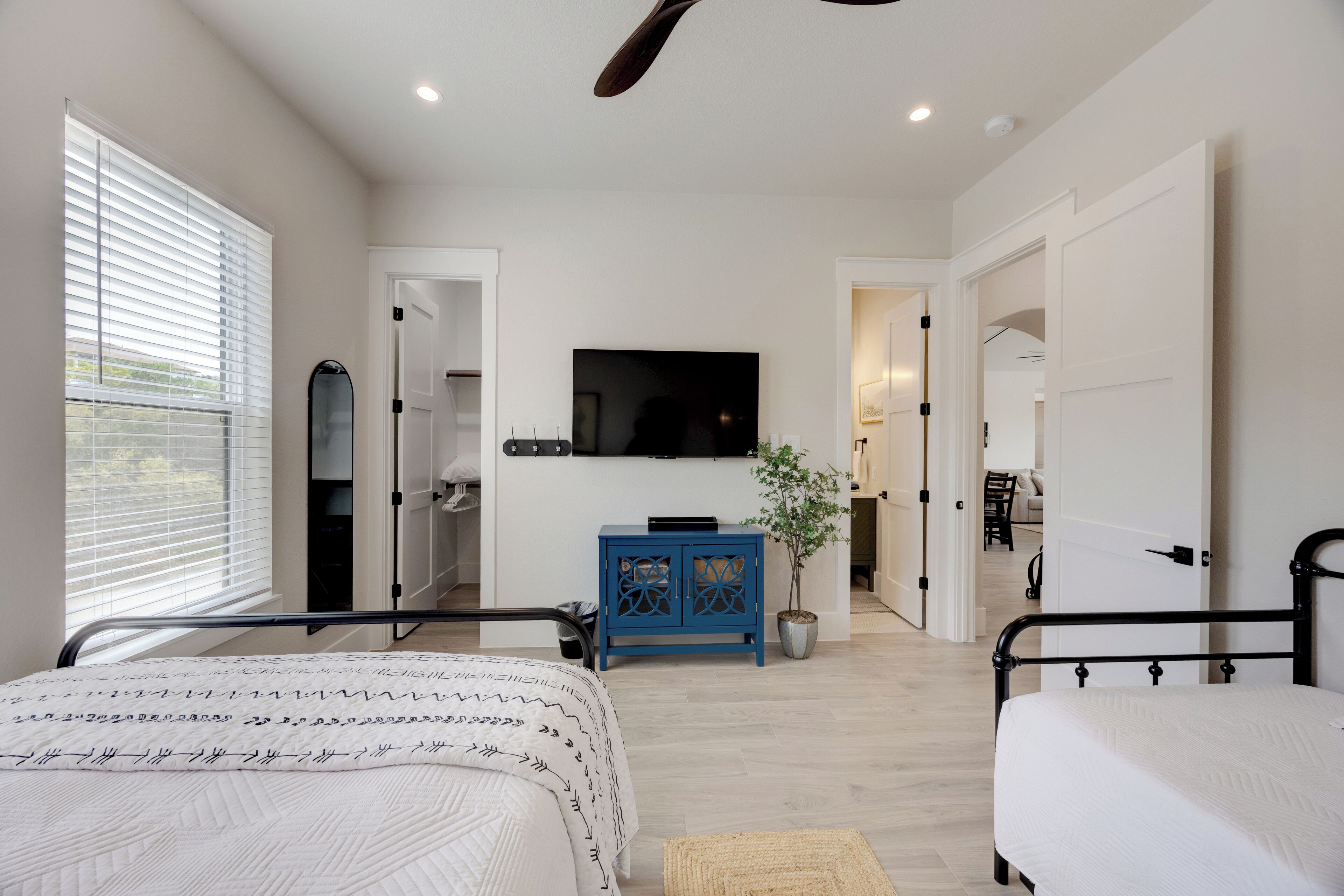 A bedroom with two beds, a TV mounted on the wall, a blue cabinet, and a potted plant.
