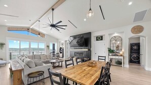 A spacious living area with a large wooden dining table, a grey sofa, and a ceiling fan. - Lakefront Retreat: Swim Spa & Backyard Lake Access! Relax & Play; 2 King Suites (Lago Vista)