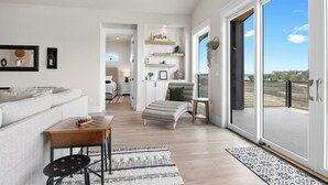 A spacious living room with a sofa, a coffee table, and a small table with a chessboard. There is a sliding glass door leading to a balcony with a view of the landscape. - Lakefront Retreat: Swim Spa & Backyard Lake Access! Relax & Play; 2 King Suites (Lago Vista)