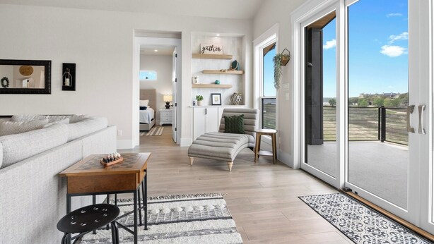 A spacious living room with a sofa, a coffee table, and a small table with a chessboard. There is a sliding glass door leading to a balcony with a view of the landscape.